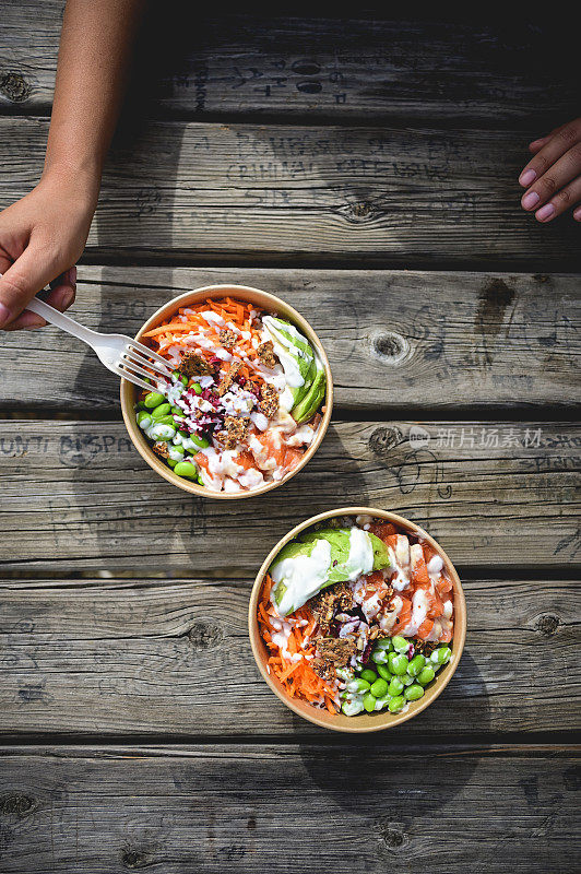 木制野餐桌上的两个poke bowl的俯视图。